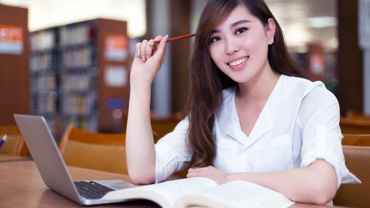 Studentin mit geöffnetem Laptop und Buch auf dem Tisch