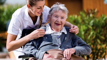 Lady as nurse supports old lady in wheelchair